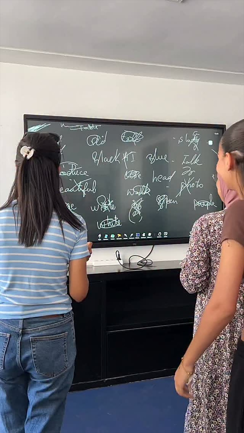 Des étudiantes rient pendant une activité devant l’écran interactif