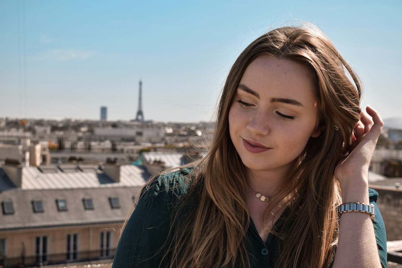 Une jeune femme souriante sur un toit de Paris, la tour Eiffel au loin
